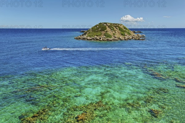 Small island Vrachonisida in front of the Grande Blue Beach in the turquoise blue sea with passing boat and blue sky with a cloud, Grande Blue Beach, Stegna, Rhodes Island, Greece