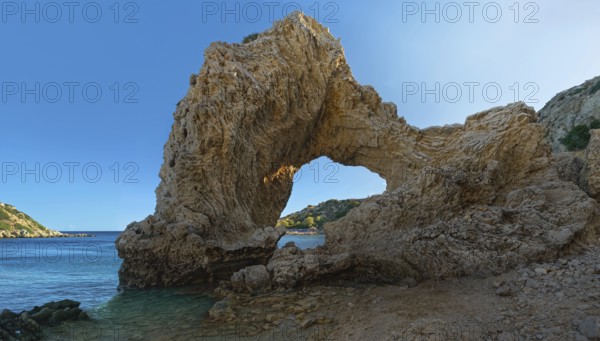 Rock arch at Grande Blue Beach under a clear blue sky in a sunny coastal landscape, Grande Blue Beach, Stegna, Archangelos, Rhodes Island, Greece