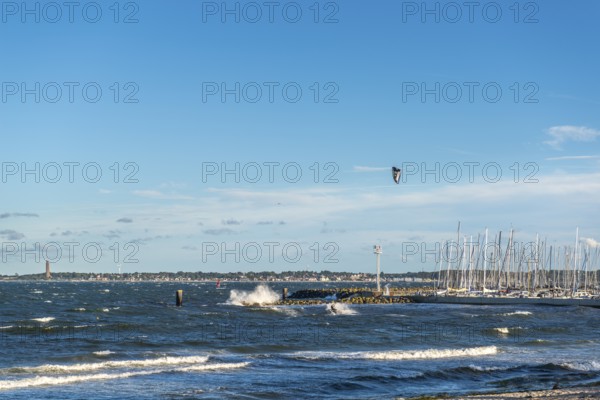Kitesurfing in the Bay of Kiel in strong winds, high swell, Strande near Kiel, Rendsburg-Eckernförde district, Kiel-Schilksee Olympic and yacht harbour, Baltic Sea Bad Laboe with tower of the naval memorial, sailing, leisure activities, water sports, spray, summer, blue sky, sunshine, Bay of Kiel, Schleswig-Holstein, Germany