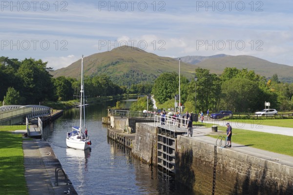 A sailing boat in the canal surrounded by green trees and mountains on a clear day, Caledonian Canal, Fort William, Scotland, United Kingdom