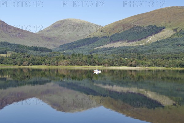 A boat on a glassy loch surrounded by mountains under a clear sky, Loch Eil, Scotland, Great Britain