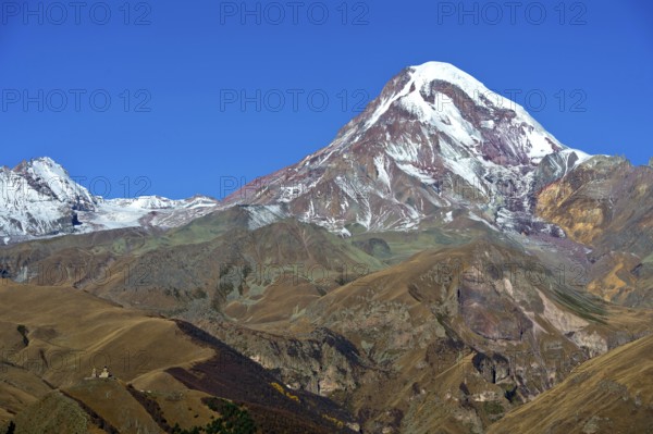 The snow- and ice-covered summit of Kasbek, with the Gergetier Trinity Church at the bottom left, Stepantsminda, Georgia