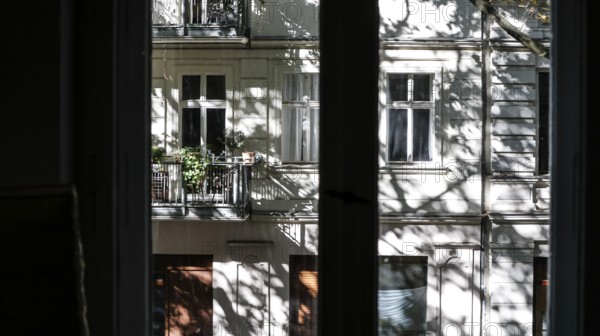 View through a window to an opposite facade of a multi-storey residential building with classical architecture and balconies with plants, shadows of leaves and branches on the house wall, Berlin, 24.09.2025, Berlin, Berlin, Germany