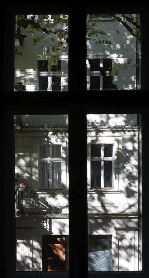 View through a window to an opposite facade of a multi-storey residential building with classical architecture and balconies with plants, shadows of leaves and branches on the house wall, Berlin, 24.09.2025, Berlin, Berlin, Germany