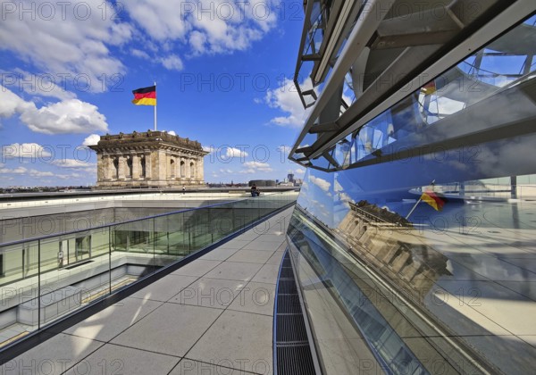 Viewing platform with a German flag in the wind on one of the corner towers and reflection in the Reichstag dome, government district, Berlin, Germany