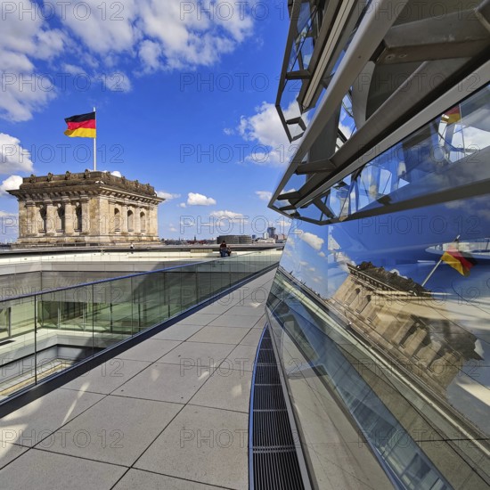 Viewing platform with a German flag in the wind on one of the corner towers and reflection in the Reichstag dome, government district, Berlin, Germany