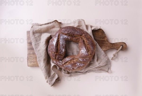 Round handmade rye bread on wooden board with linen napkin, on beige background top view, copy space