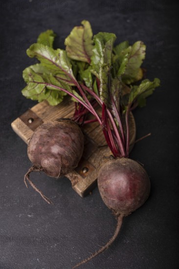 Beetroot with tops lies on a wooden board on a dark background, selective focus