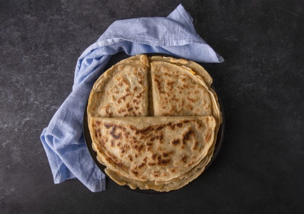 Appetizing pancakes with filling on a plate with a blue napkin, on a black background, space for text, top view