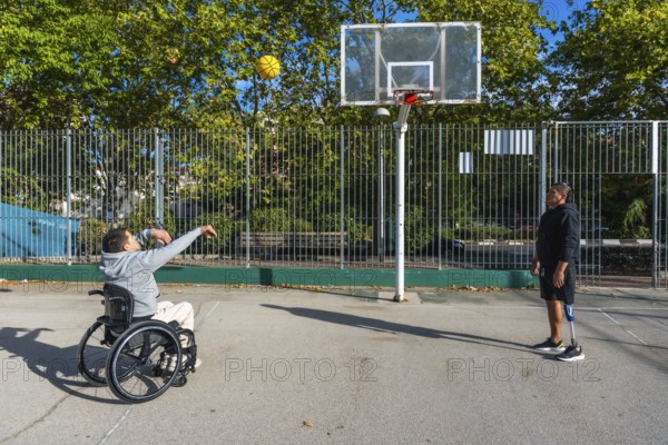 Two young men, one using a wheelchair and another with a prosthetic leg, playing basketball on an outdoor court, embracing inclusion and enjoying adaptive sports