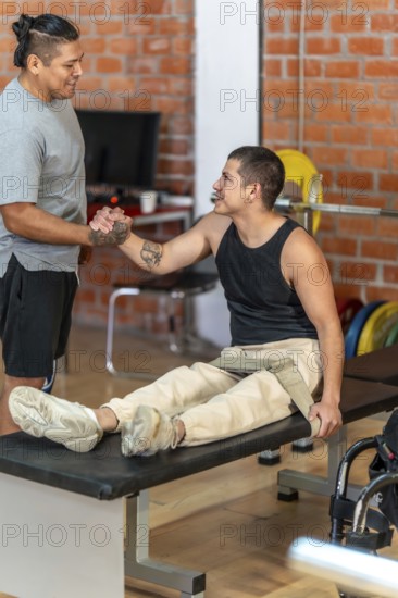 Two men shaking hands in a gym as a trainer supports an adaptive athlete with a prosthetic leg and nearby wheelchair, symbolizing determination, inclusion and teamwork during a workout