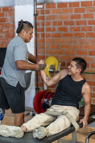 Two adult disabled men training together at a gym, one with a prosthetic leg helping the other, who is on a weight bench, focusing on teamwork, friendship, and determination