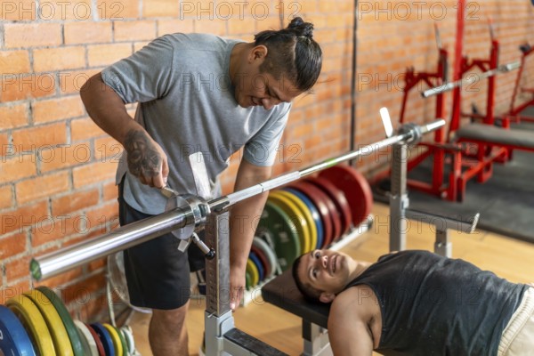 Two diverse men, one with a prosthetic limb assisting the other who is laying on a weight bench, focusing on rehabilitation and inclusive fitness training at the gym