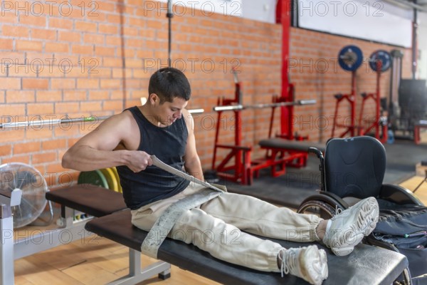Young man fitting a lifting strap onto his prosthetic leg before a gym workout, focused and determined in adaptive training, showcasing strength, perseverance and inclusion