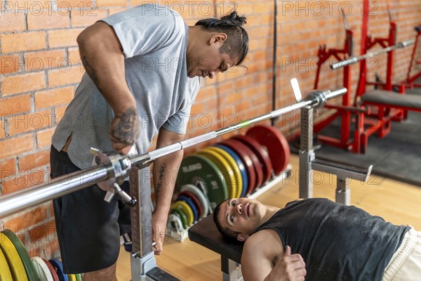 Two men in a gym, adaptive athlete bench pressing while a personal trainer spots and adjusts the barbell, showing inclusive strength training, support and focused rehabilitation
