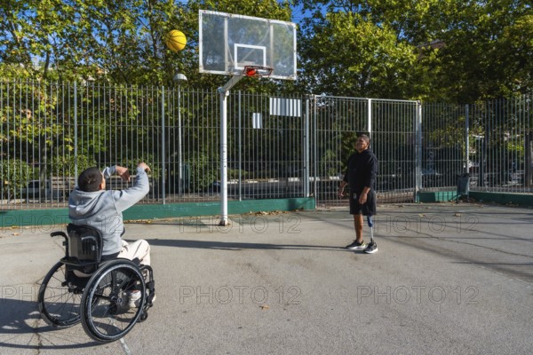 Two disabled friends are enjoying a game of basketball on an outdoor court, with one man in a wheelchair shooting the ball while his companion with a prosthetic leg watches