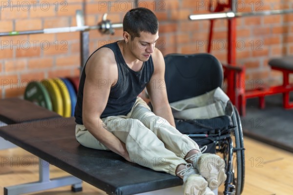 Young man with a prosthetic leg sitting on a weight bench, focusing on his leg during a workout session in an indoor gym, showcasing determination and fitness