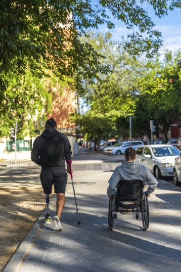 Two friends or companions, one with a prosthetic leg and using a crutch, and another person in a wheelchair, navigating a sunny city street, showing independence and inclusion