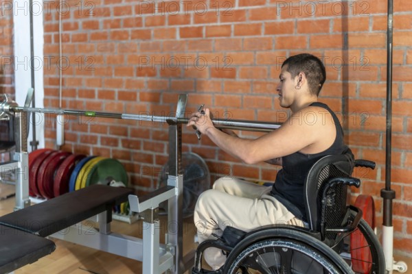 Young man in a wheelchair setting up a barbell in a modern gym, focused and determined as he trains for strength, adaptive fitness and rehabilitation progress