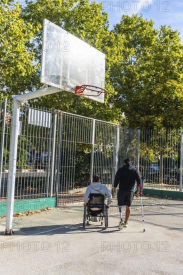 Disabled men on an outdoor basketball court, one in a wheelchair and another with a prosthetic leg and crutch walking toward the hoop, showcasing inclusion and determination