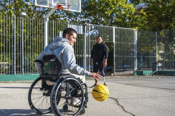 Two men experiencing disabilities, one in a wheelchair and another with a prosthetic leg, are actively dribbling a basketball on an outdoor court, enjoying sports and demonstrating active lifestyle