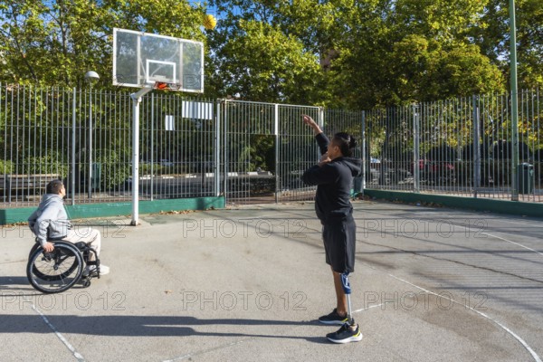 Two athletes playing basketball on an outdoor court. One sitting in a wheelchair and the other standing with a prosthetic leg. Demonstrating inclusion. Determination. And adaptive sports participation