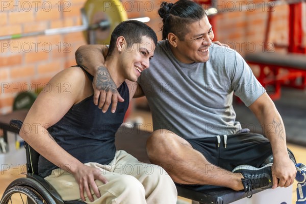 Two diverse adult men with disabilities smiling and embracing, one in a wheelchair and the other with a prosthetic leg, sharing a moment of joy and friendship at a gym