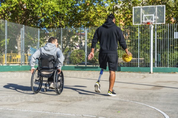 Man with prosthetic leg dribbling basketball on outdoor court while friend in a wheelchair watches, highlighting inclusion, adaptive sports, teamwork and active urban recreation