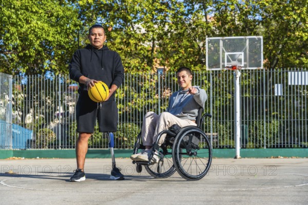 Men with diverse disabilities, one using a prosthetic leg and holding a basketball, the other sitting in a wheelchair and pointing towards the viewer, posing on an outdoor basketball court