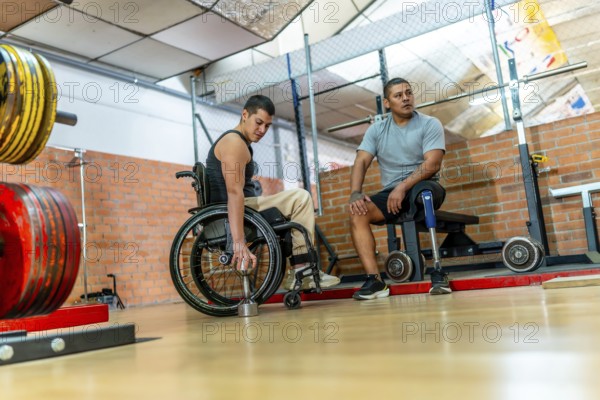 Adaptive athletes with physical disabilities engaging in training at a gym, one man in a wheelchair lifting a dumbbell and another man with a prosthetic leg resting on a bench