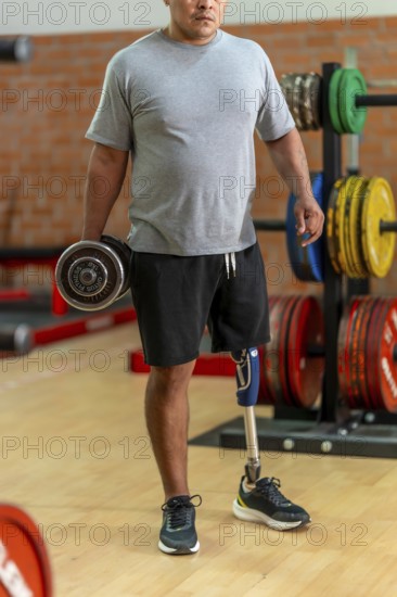 Disabled man with prosthetic leg lifting a dumbbell in gym, focused on strength training and rehabilitation, showing determination, recovery and adaptive athleticism