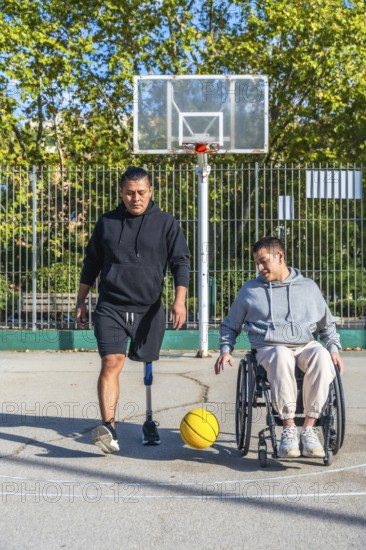 Two friends play basketball on an outdoor court, one man with a prosthetic leg, the other in a wheelchair dribbling a yellow ball, celebrating inclusion and active friendship