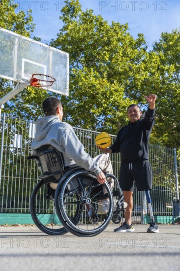 Smiling men with physical disabilities engaging in a friendly game of basketball on an outdoor court, one man using a wheelchair, the other having a prosthetic leg