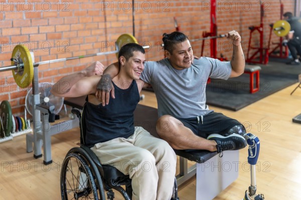 Two smiling men, one using a wheelchair and the other a prosthetic leg, warmly embracing each other at a gym, symbolizing friendship, support, and determination during their adaptive fitness workout