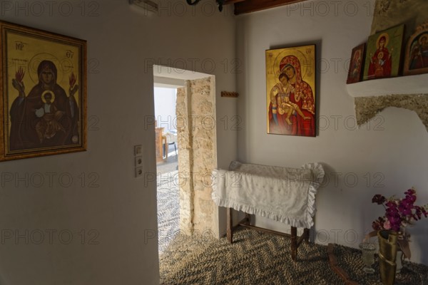 Room with religious icons of the Church of the Virgin Mary Tsambika (Kyra Psili), in warm lighting, including a white covered chest and a touch of natural light, Church of the Virgin Mary Tsambika (Kyra Psili), Archangelos, Rhodes Island, Greece