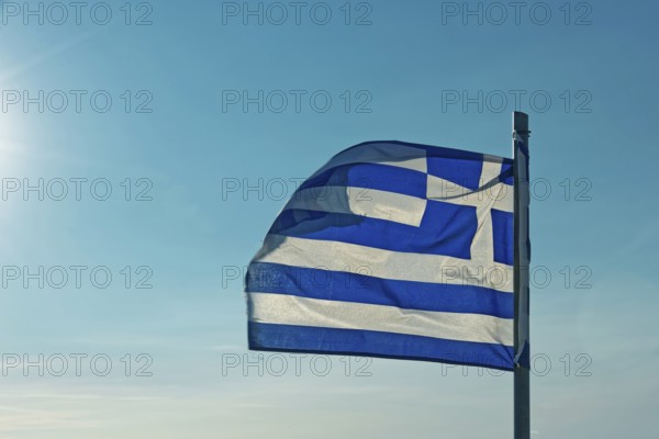 The Greek flag flies in the wind against a clear blue sky with sunshine, Church of the Virgin Mary Tsambika (Kyra Psili), Archangelos, Rhodes Island, Greece