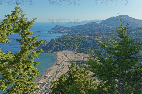 View of the Tsambika sandy beach, with mountains and blue sea, framed by green trees, Church of the Virgin Mary Tsambika (Kyra Psili), Archangelos, Rhodes Island, Greece