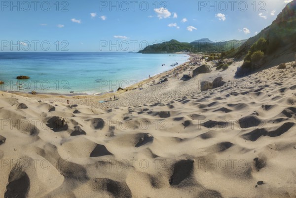 Sand dunes lead to the picturesque Tsambika beach with clear blue water and mountains in the background under a sunny sky, Tsambika beach, Archaggelos, Rhodes island, Greece