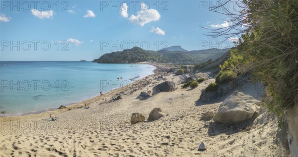 A sunny Tsambika sandy beach with clear blue water and few clouds in the sky, surrounded by rocks, Tsambika beach, Archaggelos, Rhodes island, Greece