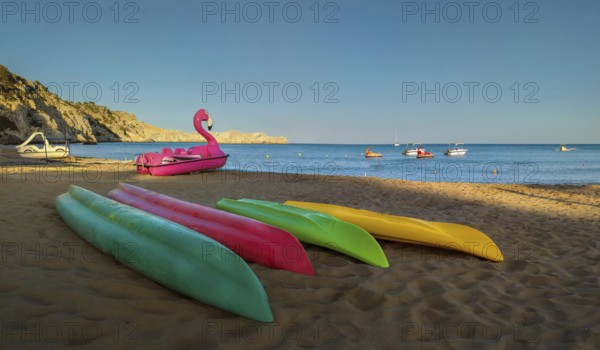Colourful kayaks lying on Tsambika sandy beach, next to a pink flamingo pedal boat, boats floating on calm sea, Tsambika beach, Archaggelos, Rhodes island, Greece