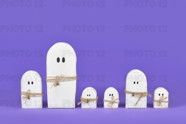 Cute wooden white Halloween ghost ornaments in a row on purple background