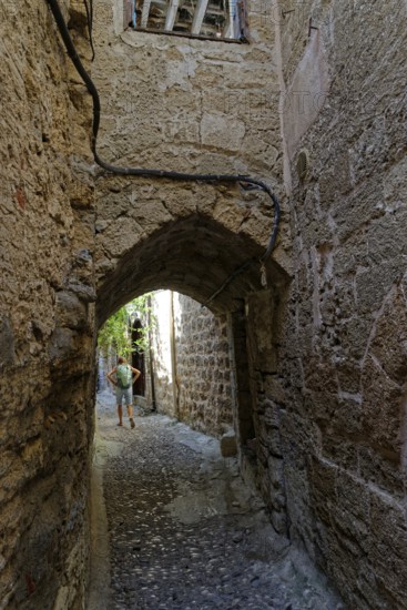 Cobbled alley with arched passageway and stone walls, a man in the background, Medieval town of Rhodes, Rhodes Island, Greece