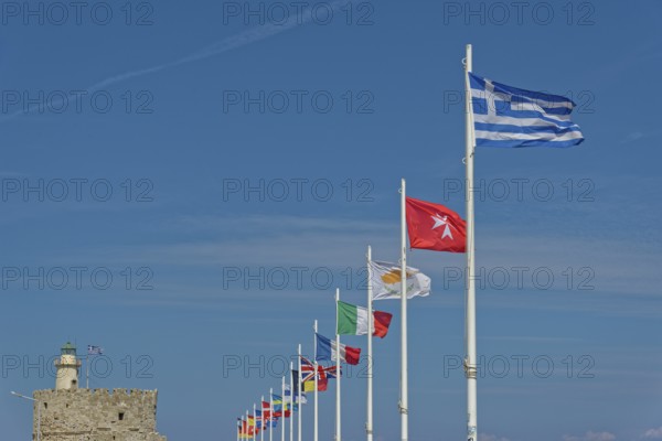 Several flags waving in the wind against a clear blue sky, including the Greek flag, Mandraki Harbour, Medieval Town of Rhodes, Rhodes Island, Greece