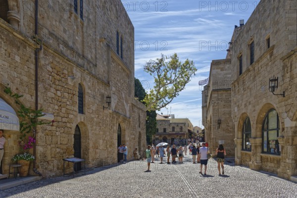 Historic old town street with cobblestones and old buildings under a blue sky full of tourists, Alexandrou Square, Medieval Town of Rhodes, Rhodes Island, Greece