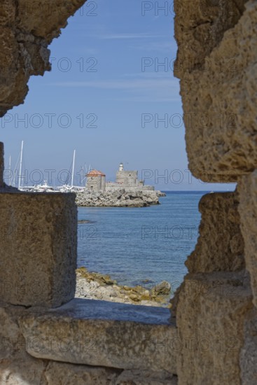 View through a wall of a medieval fort of Saint Nikolaos by the sea with sailing boats, Mandraki harbour, Medieval town of Rhodes, Rhodes island, Greece