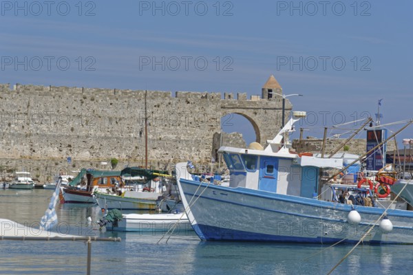 Fishing boats lying in the calm water in front of a historic city wall, Mandraki harbour, Medieval town of Rhodes, Rhodes island, Greece