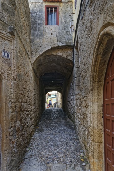 Narrow stone-paved alley with arches and high stone walls, quiet atmosphere, Medieval Town of Rhodes, Rhodes Island, Greece