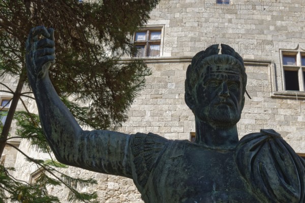 Statue of a man in ancient armour in front of a stone building with windows and trees, Grand Master's Palace, Medieval Town of Rhodes, Rhodes Island, Greece