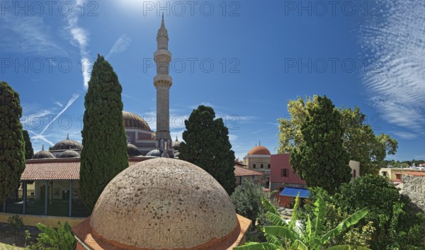 A minaret with domes and trees against a bright blue sky in a summer atmosphere, Suleiman Mosque, Medieval Town of Rhodes, Rhodes Island, Greece