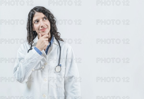 Young female doctor thinking with her hand on her chin, isolated. Thoughtful young female doctor looking up, isolated